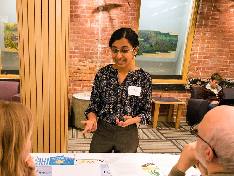 A presenter at a table in conversation with two seated attendees